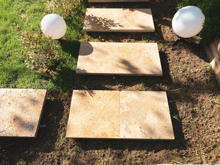 Travertine pavers laid as stepping stones in a garden with lawn, shrubs and globe lights